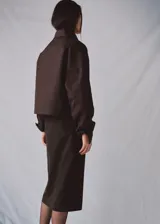 Chaqueta marrón de corte recto y diseño crop, confeccionada en mezcla de algodón y poliamida con forro interior de poliéster. Presenta cuello alto tipo embudo, doble botonadura frontal, manga larga y dos bolsillos laterales.