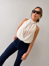Blusa negra de gasa con escote halter y diseño drapeado frontal. Presenta un corte holgado con elástico en la cintura y espalda descubierta.
