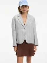 Blazer gris a rayas verticales blancas con lurex, con cuello de solapa, cierre con botón único y tajo en la espalda. Tiene un bolsillo de ojal en el pecho y bolsillos con solapa a la altura de la cadera.