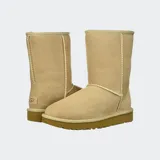 Botas de caña media UGG Classic Short II, confeccionadas en piel de oveja de doble cara color beige, con forro interior de lana suave y suela exterior liviana para mayor amortiguación.