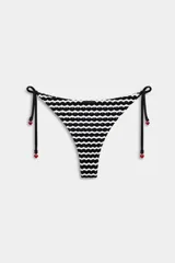 Tanga de bikini con patrón de ondas en blanco y negro, tiras laterales ajustables con pequeños dijes en forma de corazón rojo en los extremos.