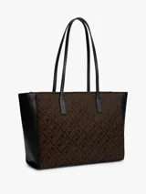 Cartera tipo tote de Tommy Hilfiger con diseño jacquard de monogramas TH en color marrón y laterales en negro. Cuenta con asas superiores fijas y logo metálico dorado en el frente.