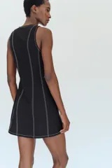 Vestido mini negro con cuello redondo y diseño sin mangas, con pespuntes en contraste y botones decorativos frontales.