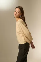 Blusa de color beige con cuello redondo y mangas largas abullonadas con puños elásticos. Presenta un corte holgado y fluido.