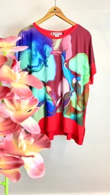 Remera poncho con estampado abstracto en tonos azul, verde y marrón sobre fondo rojo.