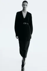 Saco largo negro de punto fino con lana, hombros caídos y ribete acanalado en nuca, puños y bajo. Sin cierre.