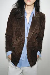 Blazer de ante color marrón, con cuello solapa, hombreras, manga larga y cierre frontal cruzado con botones. Cuenta con bolsillos delanteros de doble vivo.
