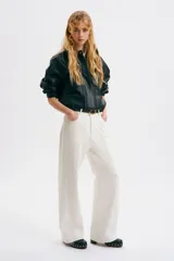 Jean de tiro regular y corte acampanado, confeccionado en denim de algodón color blanco. Presenta diseño de cinco bolsillos y detalles de costuras con ribetes bordados ondulados en el frente y los laterales.