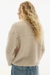 Buzo de corte oversized confeccionado en tejido de sherpa suave. Presenta cuello elevado con medio cierre frontal, hombros caídos y bolsillos insertados en el frente. Incluye canesú en la parte delantera y trasera.