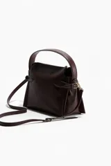 Cartera cruzada color bordó con asa superior y cierre. Cuenta con correa ajustable y extraíble, trabillas con hebilla metálica en los laterales y forro interior.