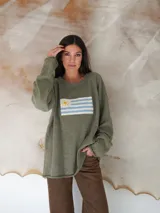 Sweater de hilo de algodón en color beige con diseño tejido de la bandera de Uruguay en el centro. Presenta cuello redondo, mangas largas y un corte holgado.