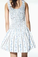Vestido corto de algodón con sección superior fruncida y pollera con vuelo, sin mangas, con escote redondo al frente y en U en la espalda, con estampado combinado de rayas y motivos florales en tonos azules sobre fondo blanco.