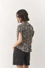 Blusa corta de manga corta con estampado en blanco y negro, cuello mao y cierre frontal con botones. Cuenta con detalle de elástico fruncido en la cintura que genera un efecto peplum.