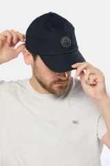 Gorro con visera de lona color verde oliva con parche circular de goma negro en el frente.