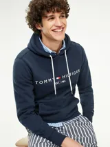 Hoodie azul marino de Tommy Hilfiger con capucha ajustable mediante cordones blancos. Presenta un bolsillo tipo canguro en la parte frontal y el logo de la marca bordado en el pecho junto a la inscripción 'EST. 1985'.