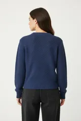 Sweater de poliéster color bordó, con cuello redondo, manga larga y diseño holgado. Presenta un patrón de punto trenzado en forma de chevrón en la parte frontal.