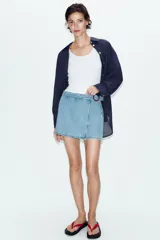 Falda pantalón cruzada de denim en color celeste, con diseño cruzado al frente, cierre frontal oculto y hebilla decorativa redonda en la cintura.