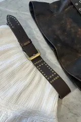 Cinturón marrón de cuero con hebilla metálica dorada y tachas doradas.