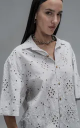 Camisa de manga corta y corte holgado con diseño de bordado broderie en toda la prenda, cuello camisero y cierre frontal de botones.
