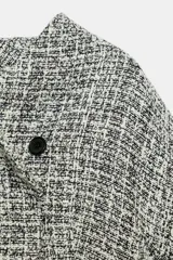 Chaqueta cruzada de estructura en tejido tweed de mezcla de hilos en tonos blanco y negro, con escote en pico, manga larga y cierre frontal con botones a presión ocultos.