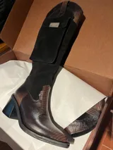 Bota alta de cuero y gamuza, color marrón con efecto texturizado en la puntera y el talón. Cuenta con taco bloque, punta cuadrada y un bolsillo lateral con solapa y placa metálica con la marca Agnès.