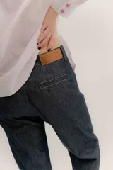 Pantalón de denim oscuro con tiro bajo y calce relajado. Presenta un cierre frontal con botones a la vista y costuras en contraste.