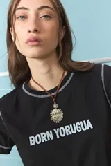 Collar con cordón marrón y dije metálico en forma de escudo con detalles grabados y sol en la parte superior.