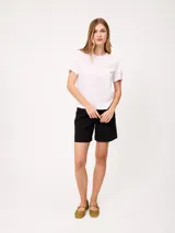 Remera blanca de manga corta con vuelta en los puños y detalle de botón dorado. Presenta cuello redondo y corte recto.