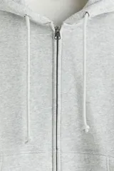 Campera con capucha de H&M, confeccionada en tejido pesado de mezcla de algodón con interior cepillado. Presenta un corte oversized, hombros caídos, cierre frontal completo, bolsillos tipo canguro y cordones ajustables en la capucha.