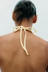 Top negro de cuello halter con lazada, escote recto y hombros descubiertos. Presenta un volante asimétrico en el lateral.