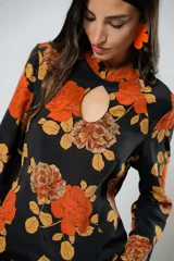 Vestido largo negro con estampado de flores naranjas y amarillas, cuello mao con abertura en forma de gota, mangas largas acampanadas con botones en los puños, tajo lateral y flecos en el ruedo.