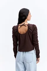 Blusa de manga larga color marrón chocolate, con diseño fruncido central ajustable mediante cordones y mangas con detalle de frunces laterales que aportan volumen.