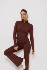 Conjunto deportivo de dos piezas color marrón, compuesto por una campera de cuello alto con cierre frontal y mangas largas con abertura para pulgar, y un pantalón de corte ajustado con terminación acampanada.