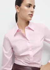 Camisa entallada de popelín de algodón color rosado, con cuello camisero, manga larga y cierre frontal oculto con botones bajo tapeta.