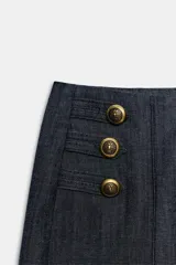 Bermuda larga de tiro alto en tejido de denim azul oscuro, con diseño de pernera recta y ancha, y detalles de botones metálicos dorados en la parte delantera.