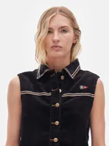 Chaleco de pana color negro con cuello camisero, cierre frontal con botones metálicos dorados, costuras contrastantes en tono claro y pequeño parche distintivo en el pecho.