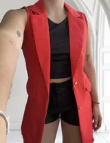 Chaleco rojo sin mangas con solapas, bolsillos delanteros y cierre con botones dorados.