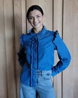 Camisa de denim azul con volados en el frente, cuello y hombros, de manga larga y corte clásico. Confeccionada en algodón.