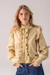 Camisa celeste con volados decorativos en los hombros, pecho, mangas y ruedo, destacados con ribetes en tono rojo. Presenta cierre frontal de botones, cuello alto y mangas largas abullonadas con puños ajustados.