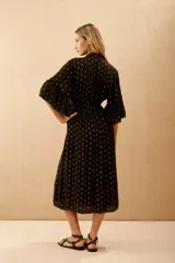 Vestido midi negro con lunares dorados, escote en V, mangas anchas al codo con bordado de lentejuelas y mostacillas. Corte amplio con ajuste elástico en la cintura y forro de algodón.