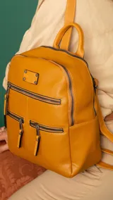 Mochila de cuero sintético en color beige con detalles en color suela. Cuenta con múltiples compartimentos frontales con cierre metálico, correas regulables y manija superior.