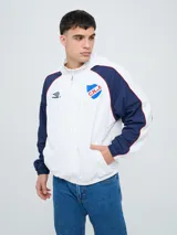 Campera deportiva Umbro del Club Nacional de Football, modelo Venti, para hombre. Diseño en color blanco con mangas azules y detalles de líneas rojas. Cuenta con capucha con cordón ajustable, cierre frontal y bolsillos. Presenta el logo de Umbro y el escudo del club bordados en el pecho.