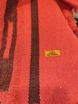 Poncho negro de hilo de algodón, con diseño geométrico tejido en tonos bordó y beige, detalles en cuerina marrón en el cuello y flecos en el ruedo.