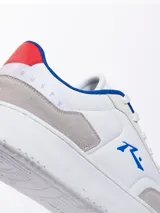 Championes urbanos blancos con detalles en gris, azul y rojo. Presentan el logo de la marca en el lateral y cordones blancos.
