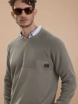 Sweater de punto verde militar con cuello redondo, mangas raglán y un pequeño bolsillo en el pecho con detalle de parche con logo.