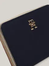 Billetera mediana de Tommy Hilfiger en color azul marino, con cierre de cremallera perimetral. Presenta el monograma TH metálico en dorado en la parte frontal y un tirador de cierre con los colores distintivos de la marca.