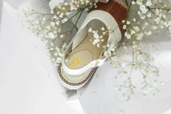 Sandalias de cuero con diseño bicolor, combinando una franja de cuero blanco texturizado y una franja de cuero marrón con textura de reptil. Poseen suela track dentada, puntera abierta y tira ajustable con hebilla en el talón.
