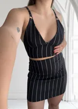 Conjunto de top y pollera negra con rayas verticales blancas. El top es corto con breteles finos y escote en V. La pollera es mini y ajustada.