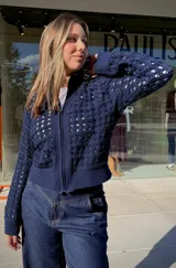 Chaqueta de punto calado color azul marino, con cierre frontal completo, cuello alto y puños tejidos en punto elástico.