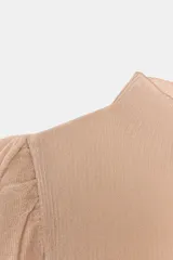 Top de punto en color beige con cuello subido y mangas largas. Presenta un diseño ajustado en el cuerpo con mangas abullonadas en los hombros que combinan una textura semitransparente.